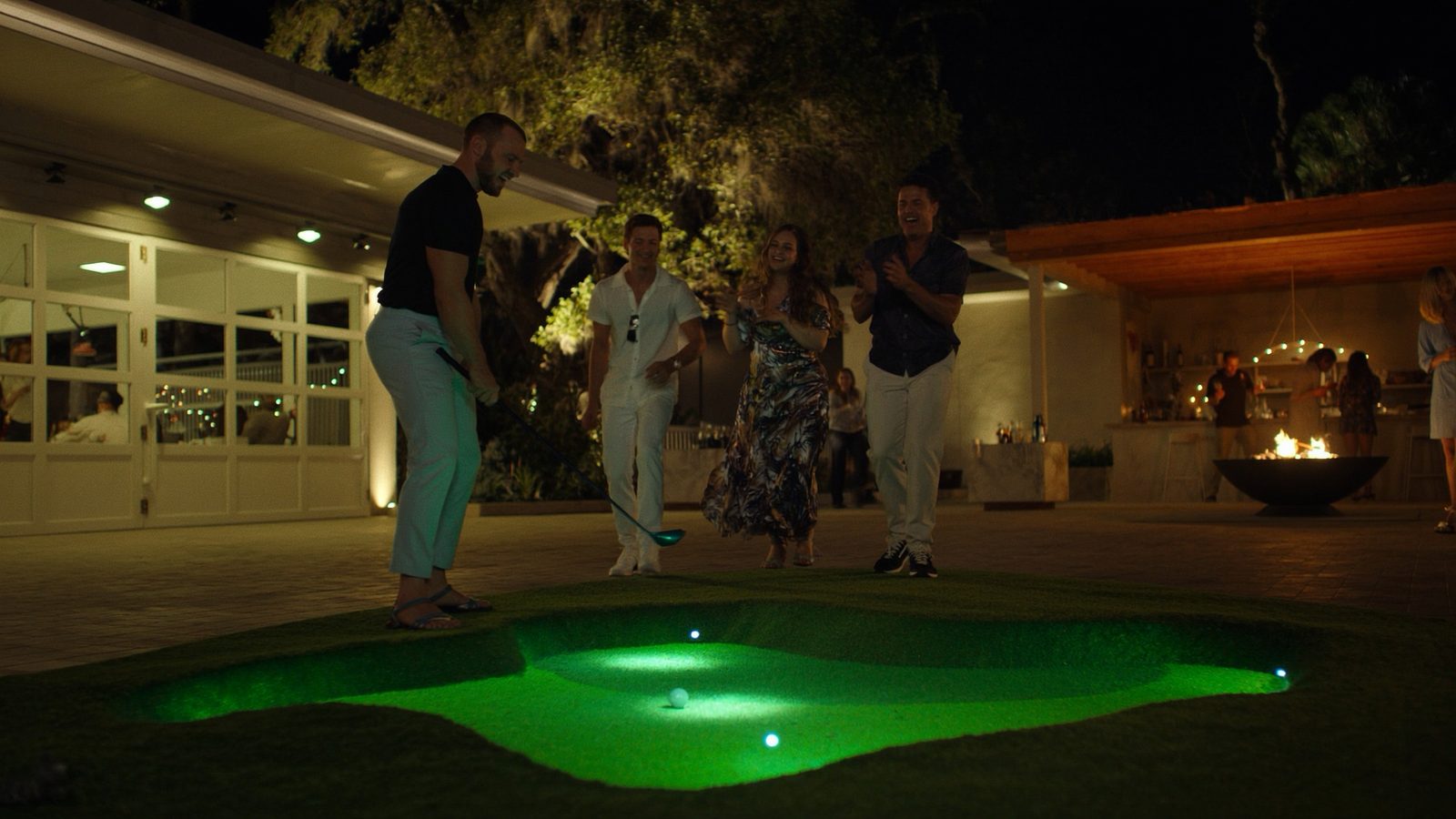 People putting on a lit green by the clubhouse at night